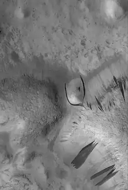 D. Dark slope streaks in Phlegra Dorsa region as seen by MOC. The streak near the center of image has been diverted around a small hill. The image is about 3&nbsp;km (1.9&nbsp;mi) across.