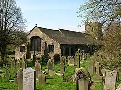 A long, low-roofed church building, with a tower in the background and the building itself set amongst gravestones