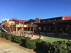 2 storey brick school building with play equipment in foreground