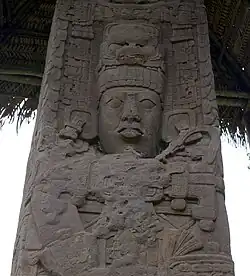 Close up of upper portion of an intricately carved stela, showing the face of a king with elaborate headdress and jewellery