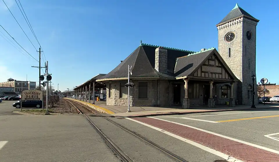 A stone Romanesque railway station with a square clock tower next to a single track