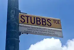 yellow street sign with maroon text mounted on metal light pole
