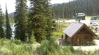 A lake cabin near a lake, with a parking lot and dirt road behind the cabin