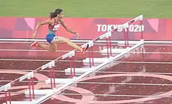 Photo of Sydney McLaughlin while jumping over a hurdle on a red athletics track
