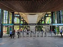 Picture of Rouse Hill station. The station has elevated platforms. The picture was taken below the platforms at the ground level concourse, which is surrounded by green-coloured glass on the exterior.