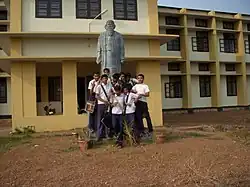 Students in official school uniform in front of the statue of Tagore at the entrance of the school.