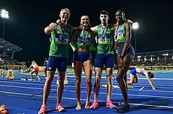 Photo of Thomas Barr, Sharlene Mawdsley, Cillin Greene, and Rhasidat Adeleke wearing their national kits in green and blue, having medals around their necks, and standing on a blue track