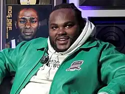 Tee Grizzley in 2024 in an interview sitting next to a vinyl of Mos Def’s Black on Both Sides album.