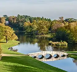 A view along a winding body of water, with a white Gothic folly at the far end and a five-arch bridge in the foreground