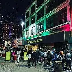 Exterior shot of an historic 4 story white building on a block in Baltimore with a crowd of people waiting to enter the haunted attraction. A green sign on the front reads: The Nevermore Haunt