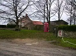 A red post-box and a red telephone box, with trees and a small collection of buildings beyond