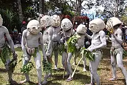 A group of people covered in white body paint with large white masks covering their entire head