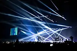 A darkened stage with a rectangular screen and multiple beams of light.