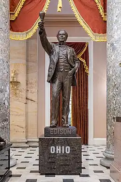 A brown bronze statue of Tomas Edison. He is wearing a suit and holds his right hand high up, with a lightbulb. On the pedestal is the word "OHIO".