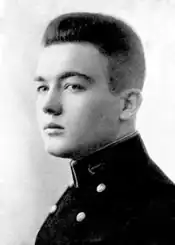 Profile of a young white man with hair thick on top and short at the sides, wearing a dark jacket with two columns of buttons down the chest and an anchor emblem on the side of the upright collar.