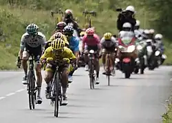 A small group of descending riders led by Julian Alaphilippe wearing a yellow jersey in an extreme tuck position