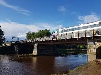 A train crossing a bridge with one stone pier of the bridge in the water of the river