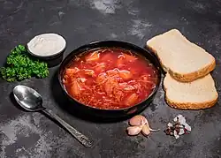 A bowl of red borscht with two pieces of bread, sour cream, and garlic