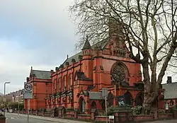 A red brick church with a rose window, a bellcote and a series of gabled buttresses