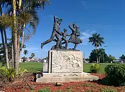 A statue depicting a family running from the storm. The concrete base below it shows a tidal wave washing away homes, telephone poles, animals, and people