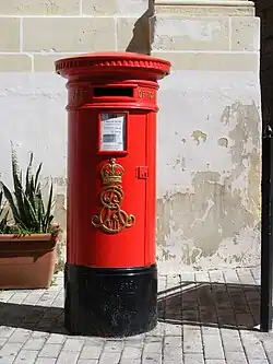 A red pillar box in Vittoriosa, Malta. In the 1980s, royal cyphers were ground off the pillar boxes in Valletta and Floriana, but most others remained intact.[26]