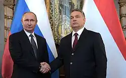 Vladimir Putin and Viktor Orbán meeting in 2017, shaking hands in front of a Russian and a Hungarian flag