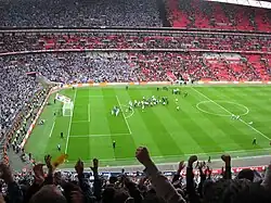 A full football stadium, with spectators in the left half wearing blue, and those in the right half wearing red