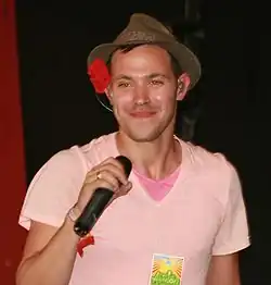 A man in a pink t-shirt smiling and holding a microphone