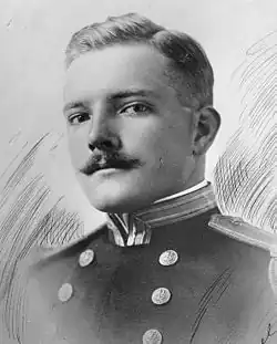 Head and shoulders of a white man with a neatly trimmed mustache wearing a military jacket with shoulder boards and two columns of buttons down the chest.