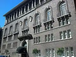 A large brick building with an elaborate front entrance, balconies, and columns on the upper floors