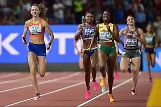 Frontal photo of five athletes holding a baton while running on a red athletics track