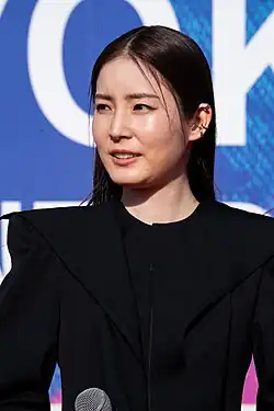 waist up portrait of Renbutsu in black outfit facing to left of audience