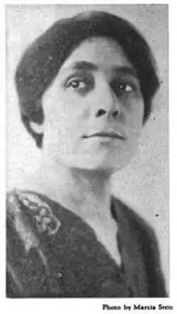 Photograph of a woman with dark hair and eyes, wearing a dark v-necked top or dress.